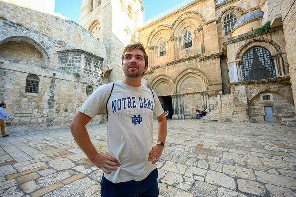 A Notre Dame student standing in a tiled courtyard, studying abroad.